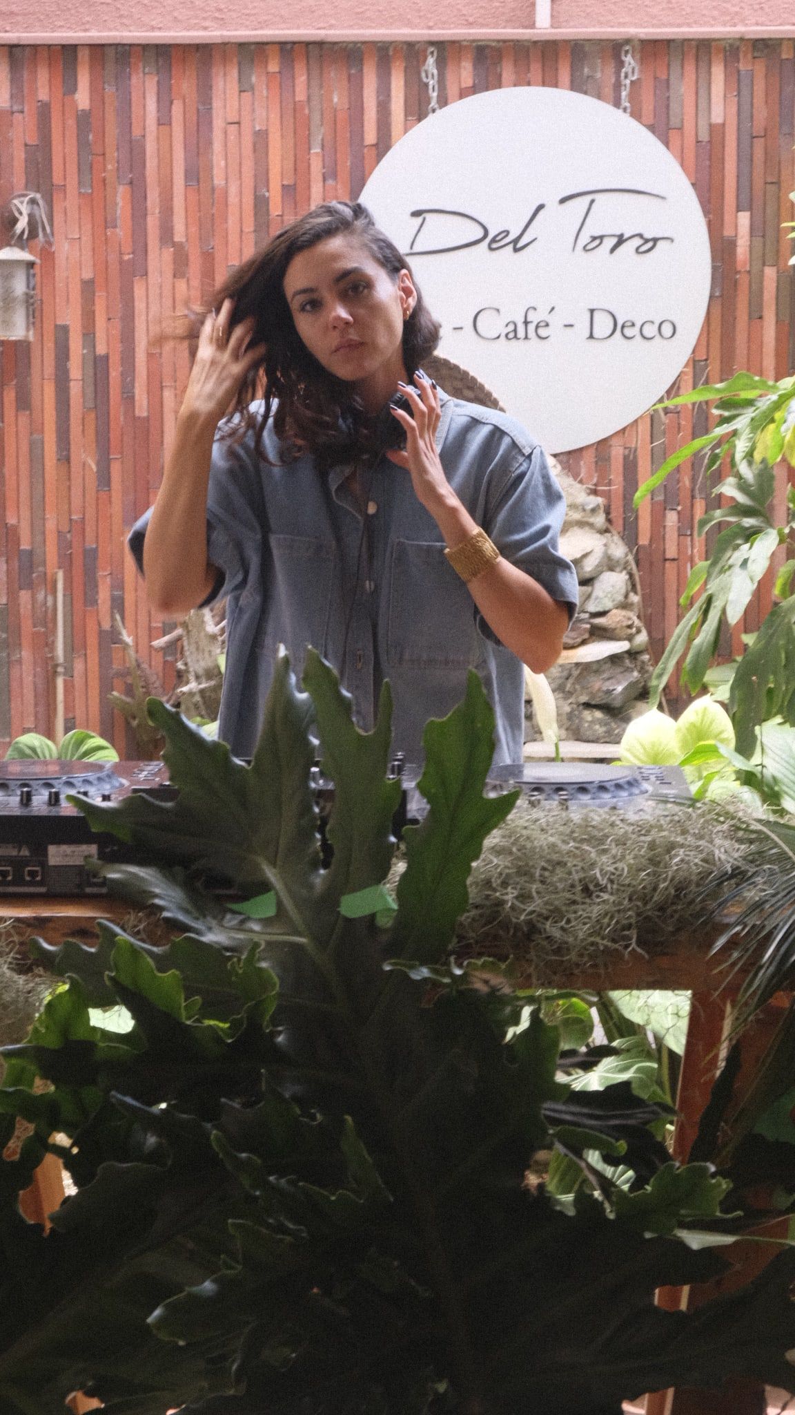 Una DJ se acomoda el pelo entre las plantas del jardín, frente al letrero redondo de la casa