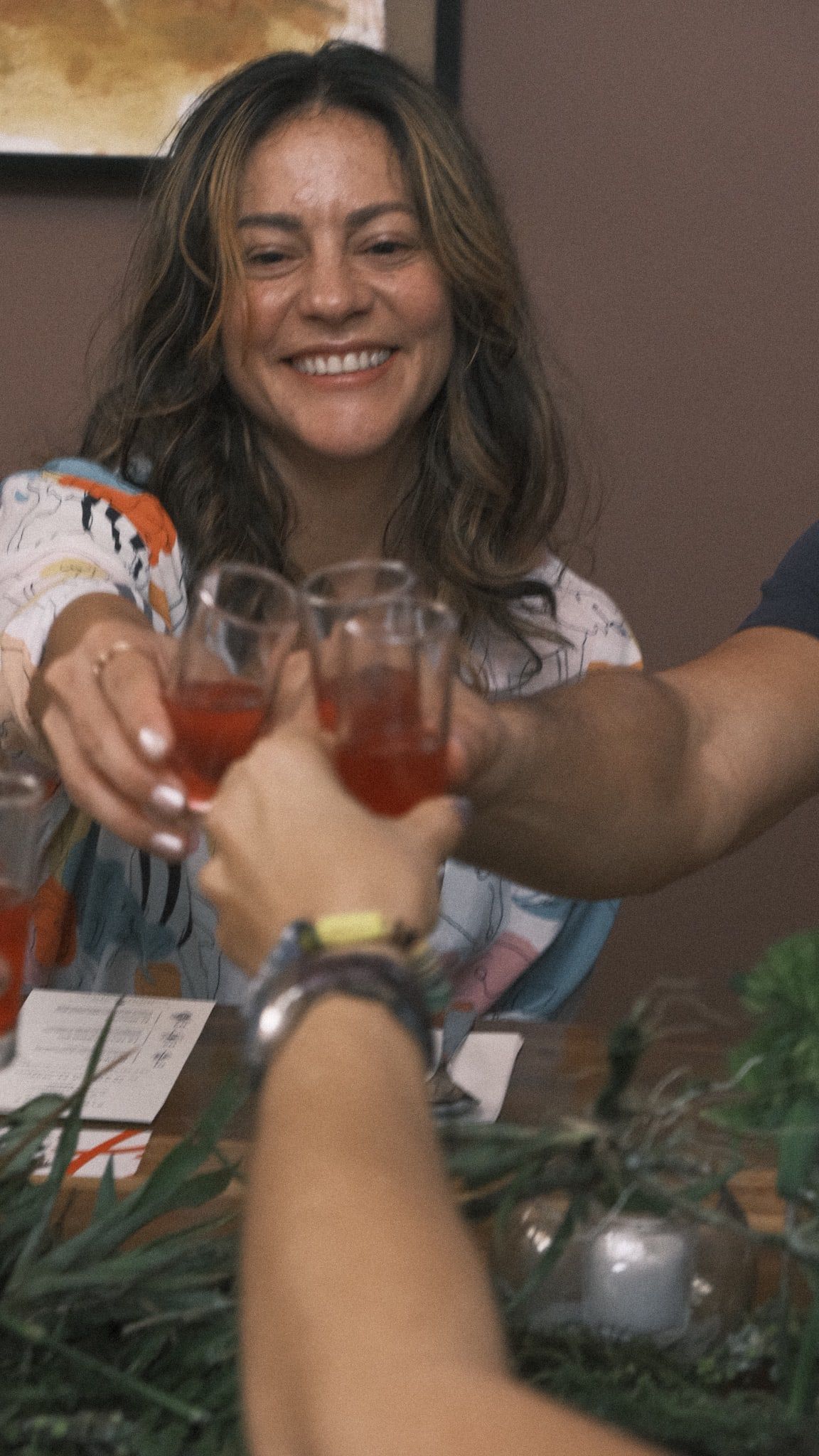 Tres manos brindan con copas de bebida roja sobre la mesa decorada con hojas