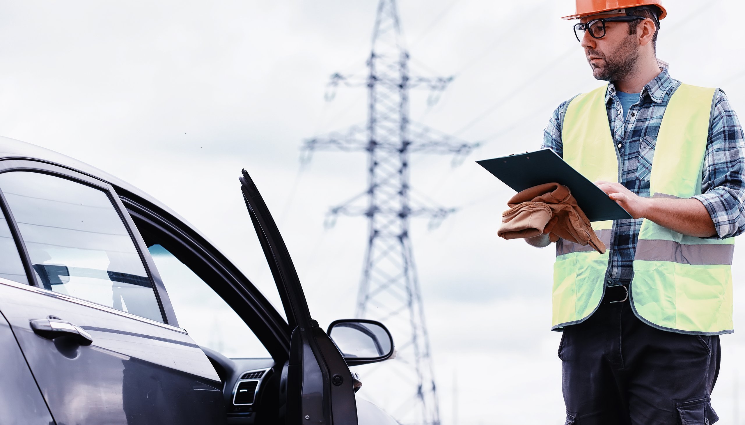 a man in a hard hat holding a clipboard next to a car
