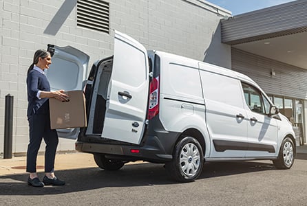 a woman holding a box and opening the door of a van