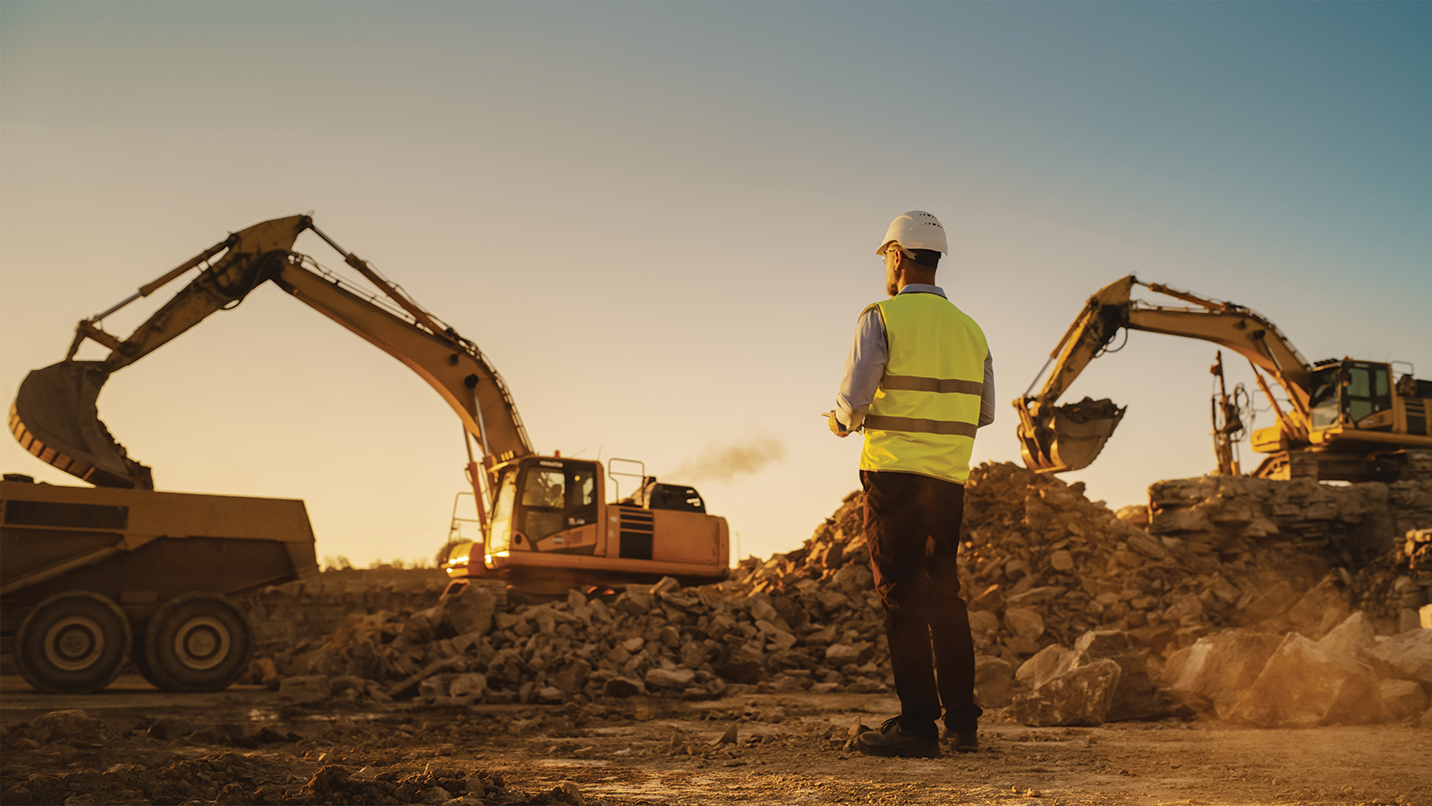 Construction worker surveying two excavators on a job site.