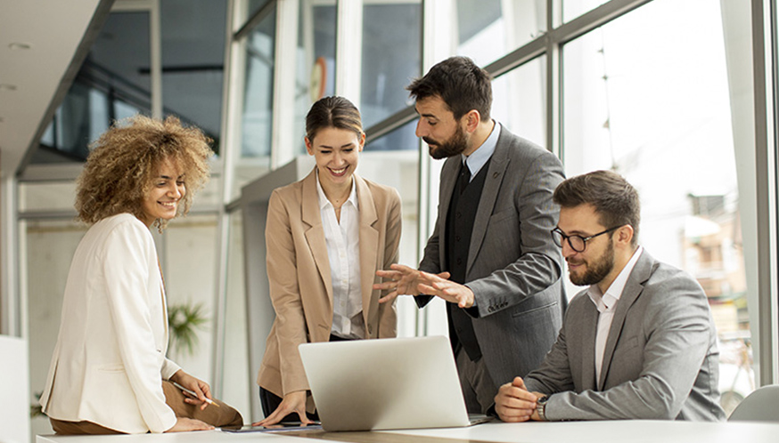 a group of people standing around a table looking at a laptop