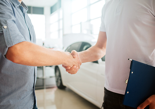 a man shaking hands with another man in a car dealership