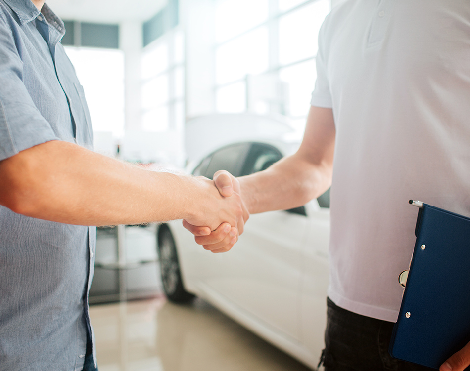 a man shaking hands with another man in a car dealership