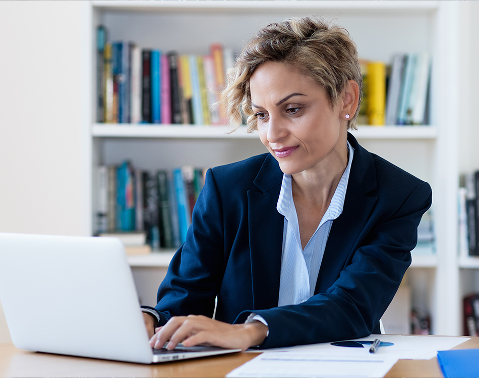 a woman in a suit sitting at a desk using a laptop