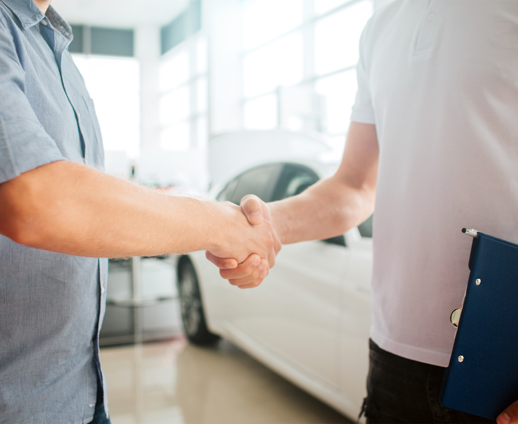 a man shaking hands with another man in a car dealership