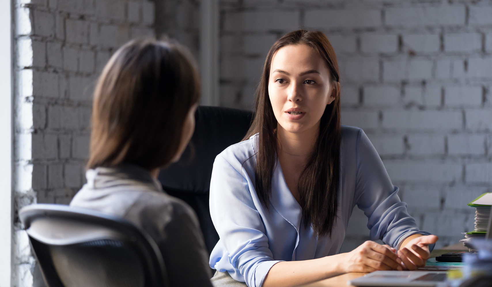 a woman sitting at a table talking to another woman
