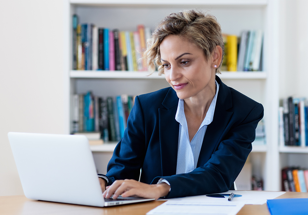 a woman in a suit sitting at a desk using a laptop