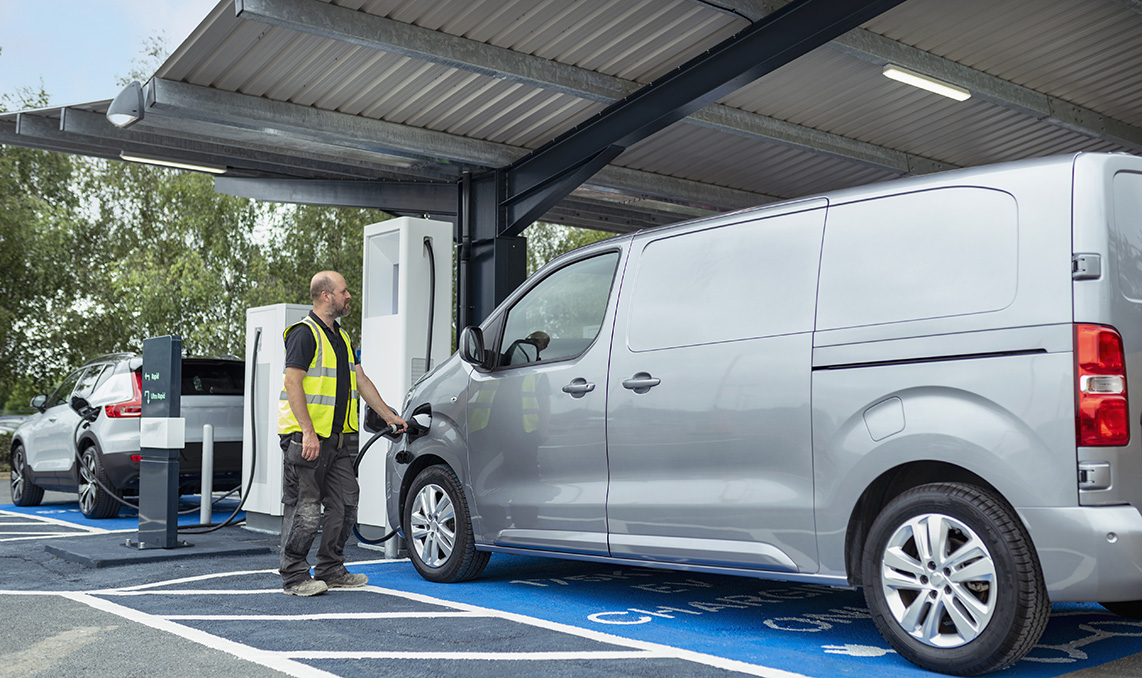 Ein Mann lädt an einem Bahnhof einen grauen Transporter auf