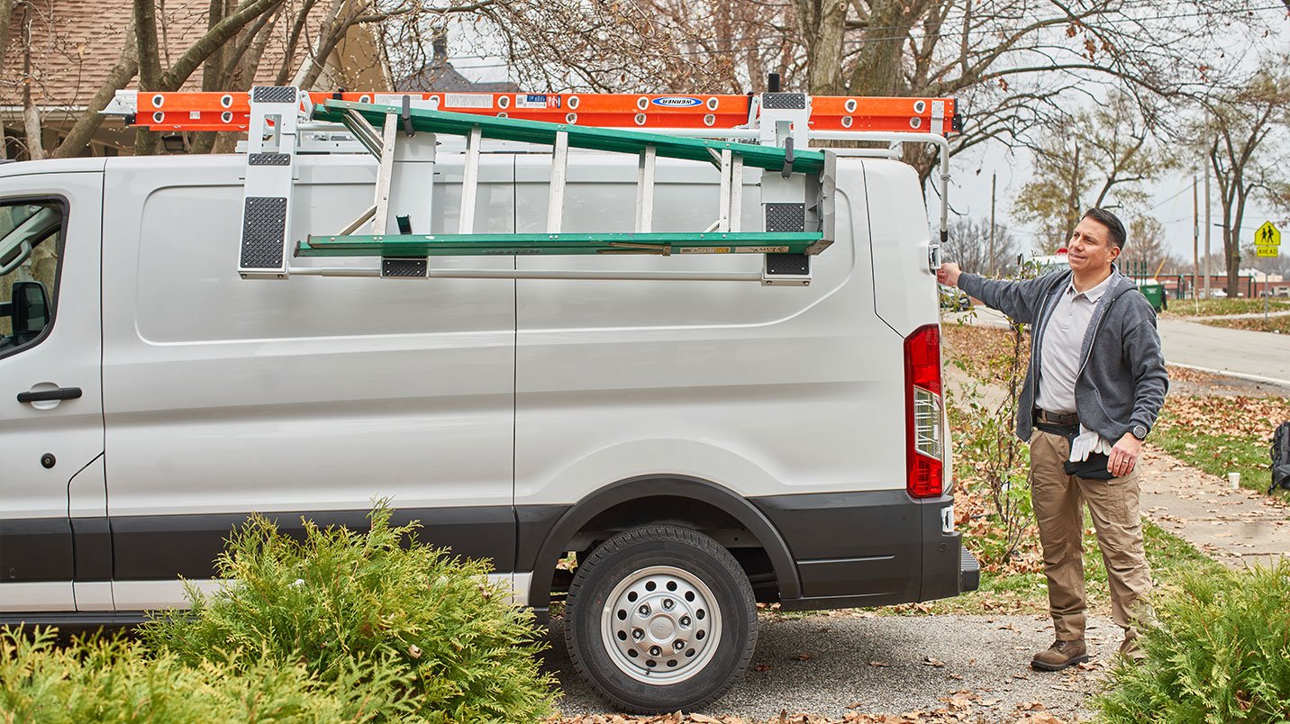 a man standing next to a ladder on the back of a van