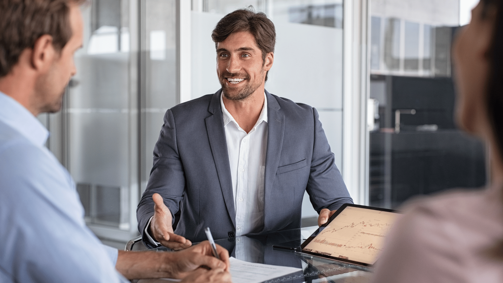 a man in a suit sitting at a table with a tablet and a pen