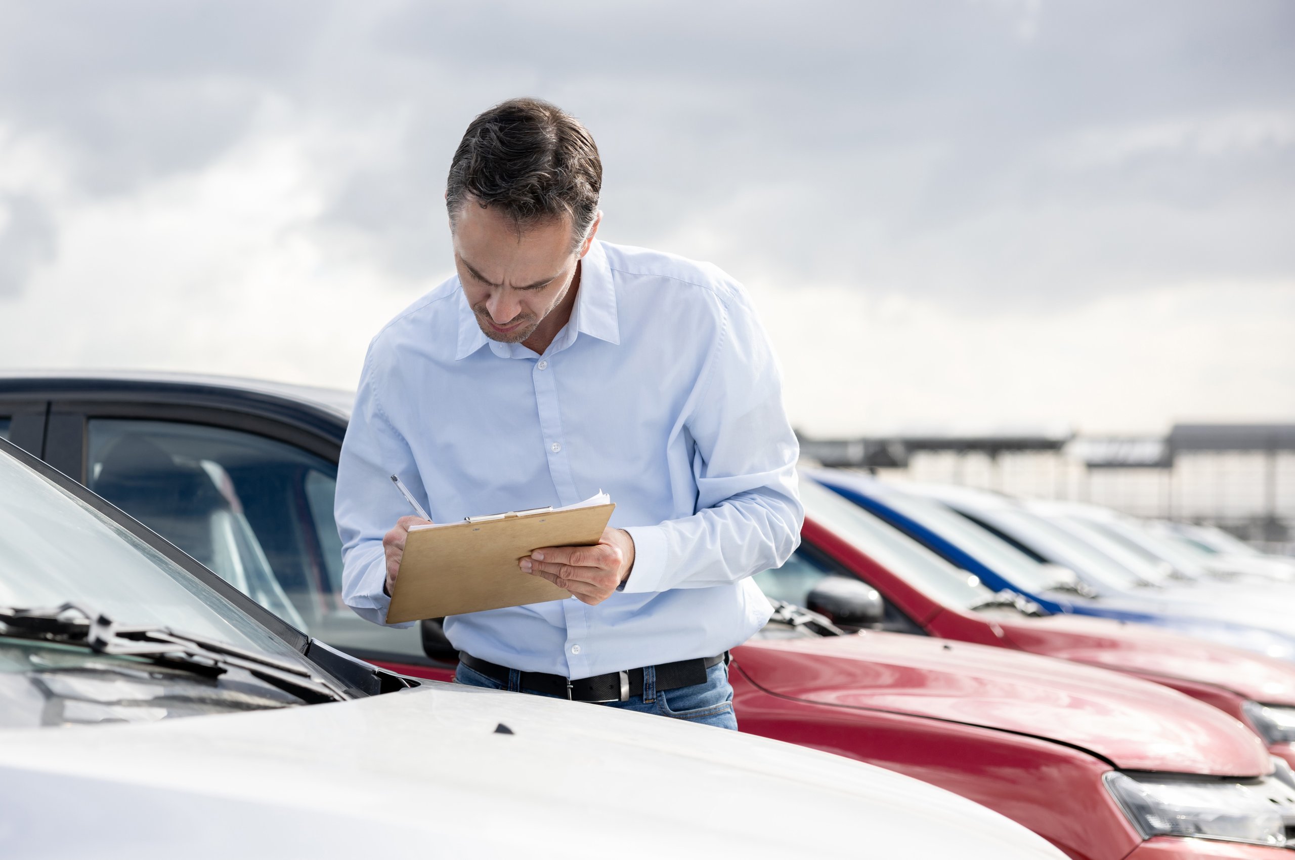 a man writing on a clipboard next to a row of cars