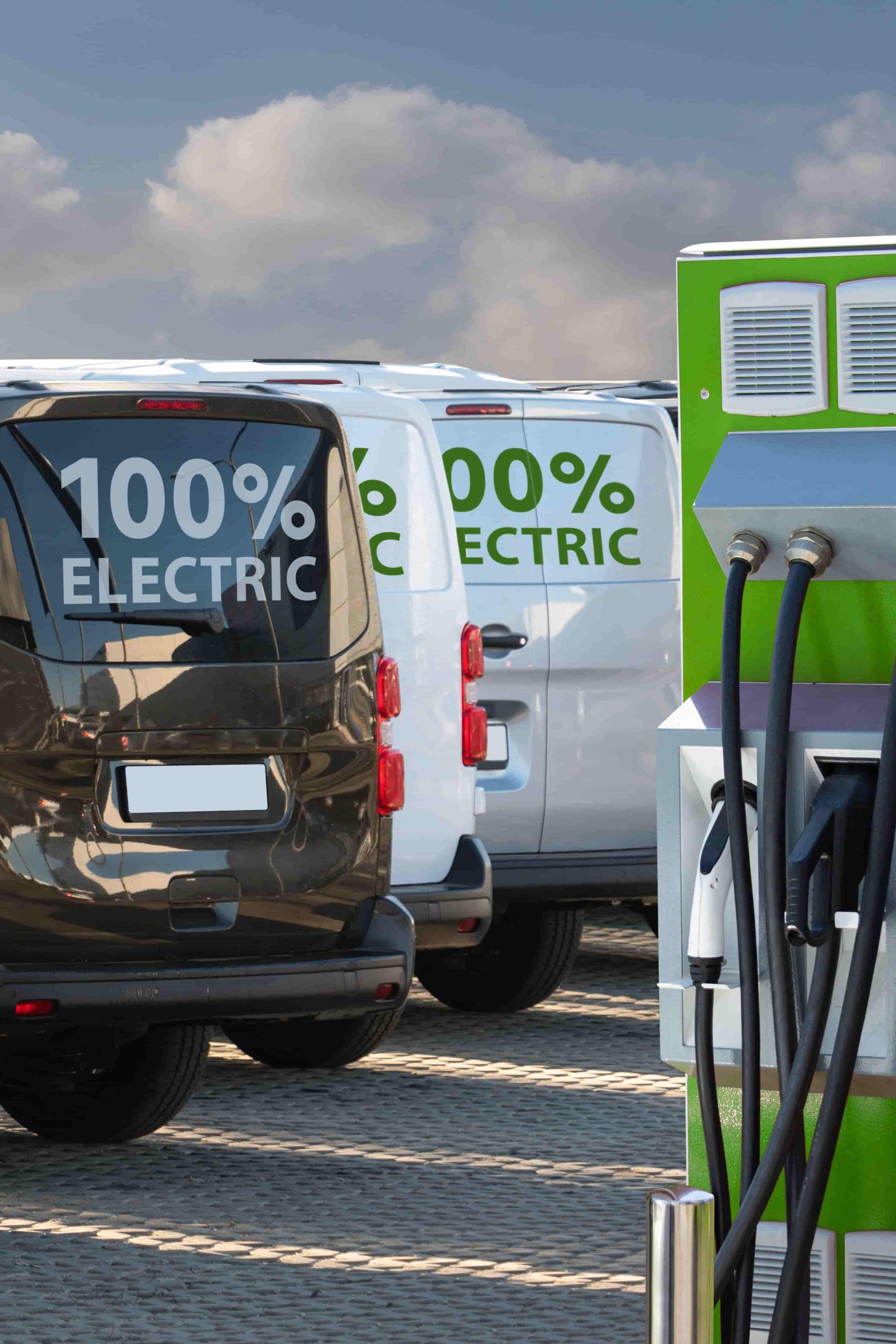 Mehrere elektrische Kleintransporter an Ladestationen auf einem Firmenparkplatz als Beispiel für die schrittweise Elektrifizierung eines Fuhrparks.