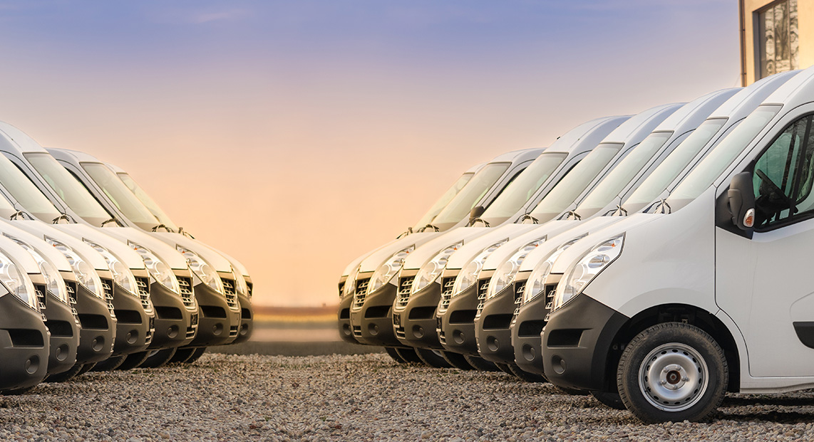 Two rows of white cargo vans facing each other in a lot