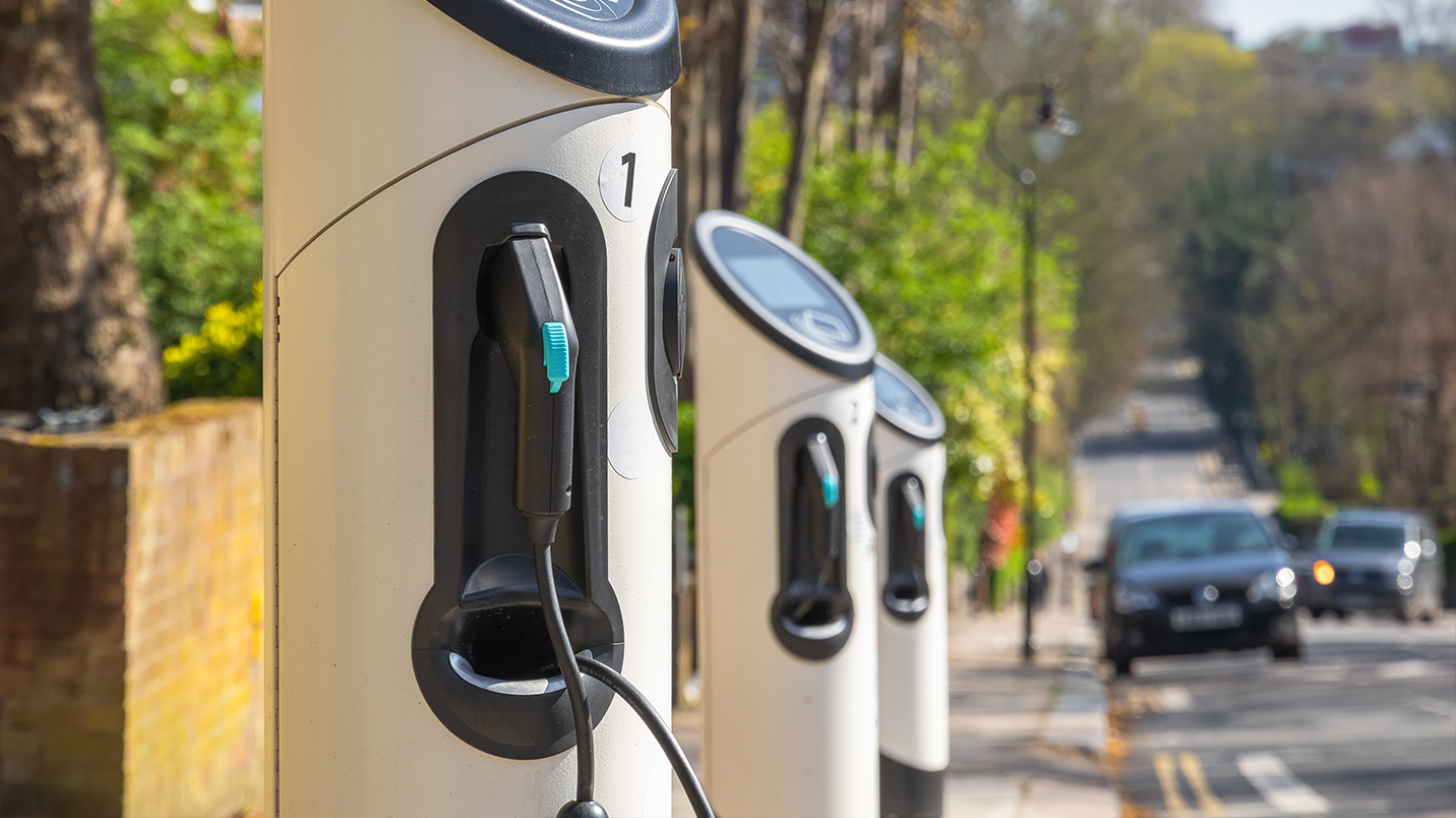 A row of electric car charging stations on the side of a tree lined street.