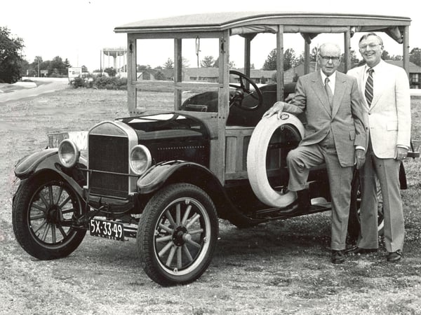 Black and white picture of two men standing next to a car