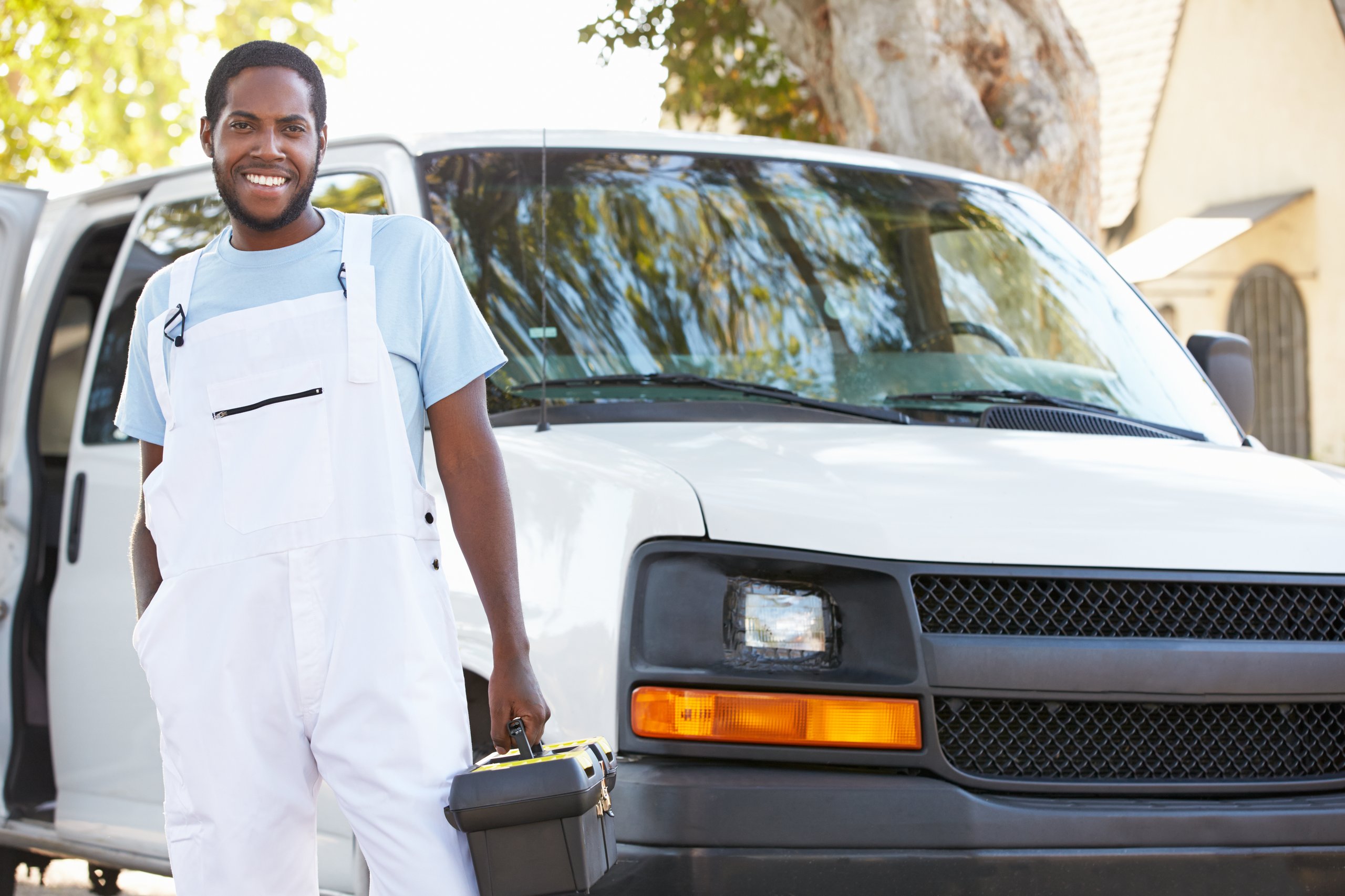 a man in white overalls holding a toolbox next to a white van