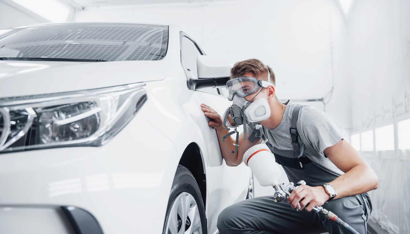 a man wearing goggles and a mask painting a car