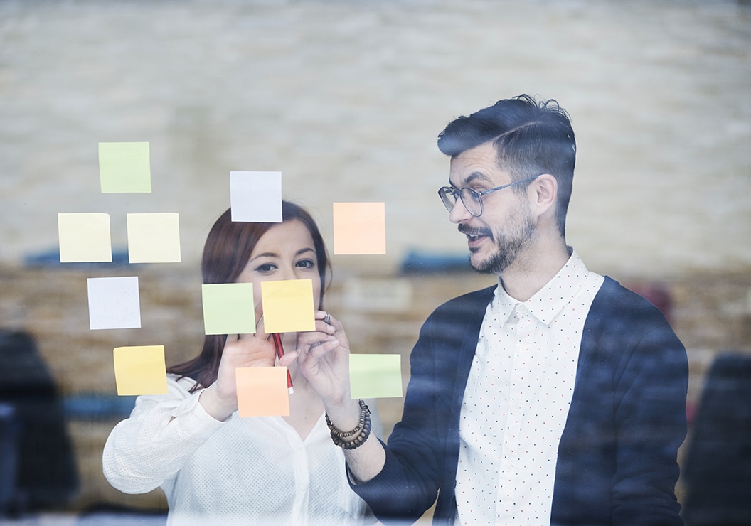 a man and woman looking at sticky notes on a glass wall