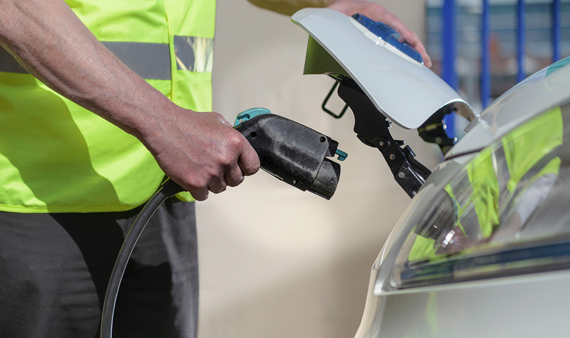 a person holding a charging cable to a car