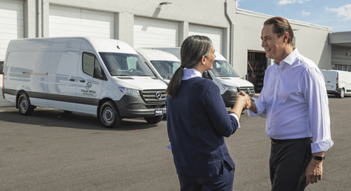 a man and woman shaking hands in front of white vans