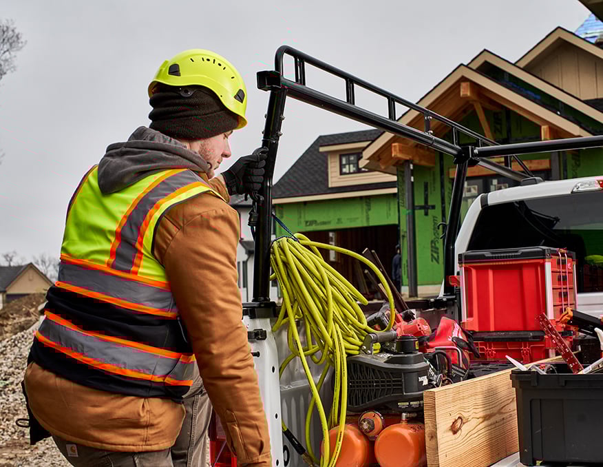 A construction worker holding onto a truck rack