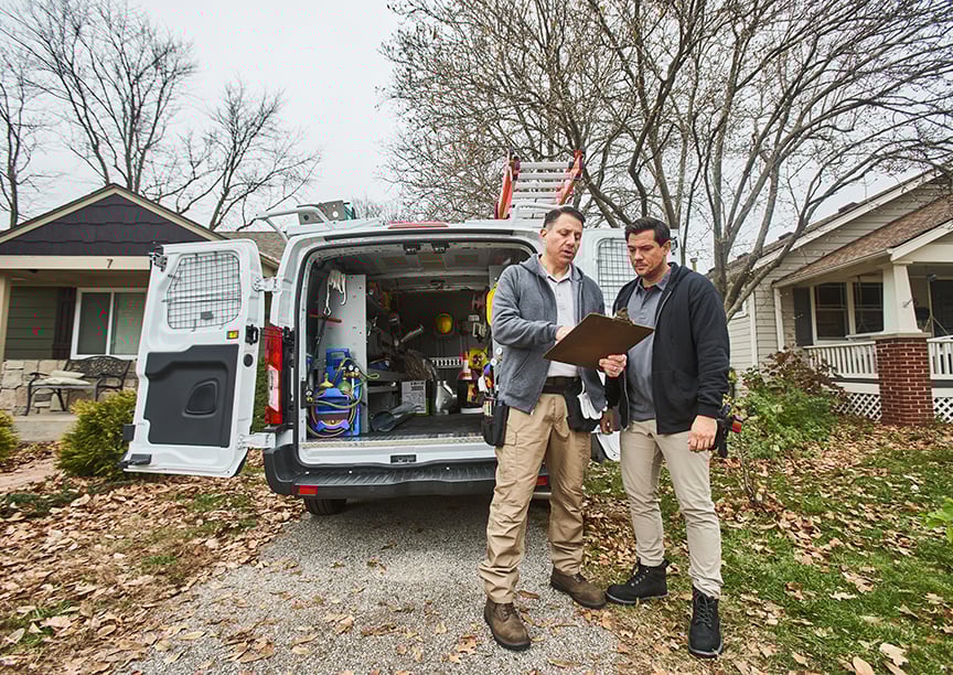 Two people looking at a tablet in front of an upfitted light-duty van