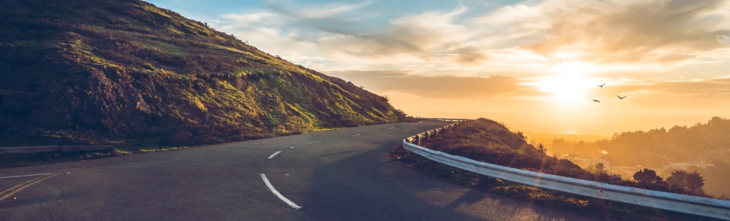 a road with a fence and grass hill