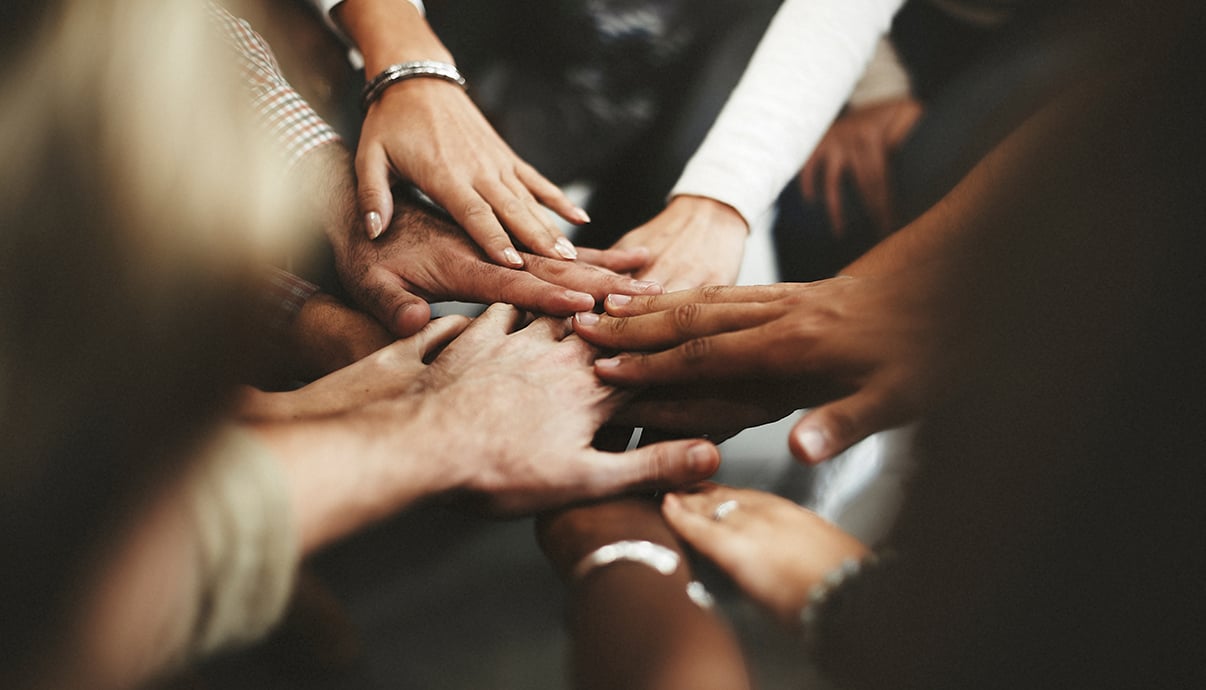A team huddle with their hands stacked in the middle for a pep talk.