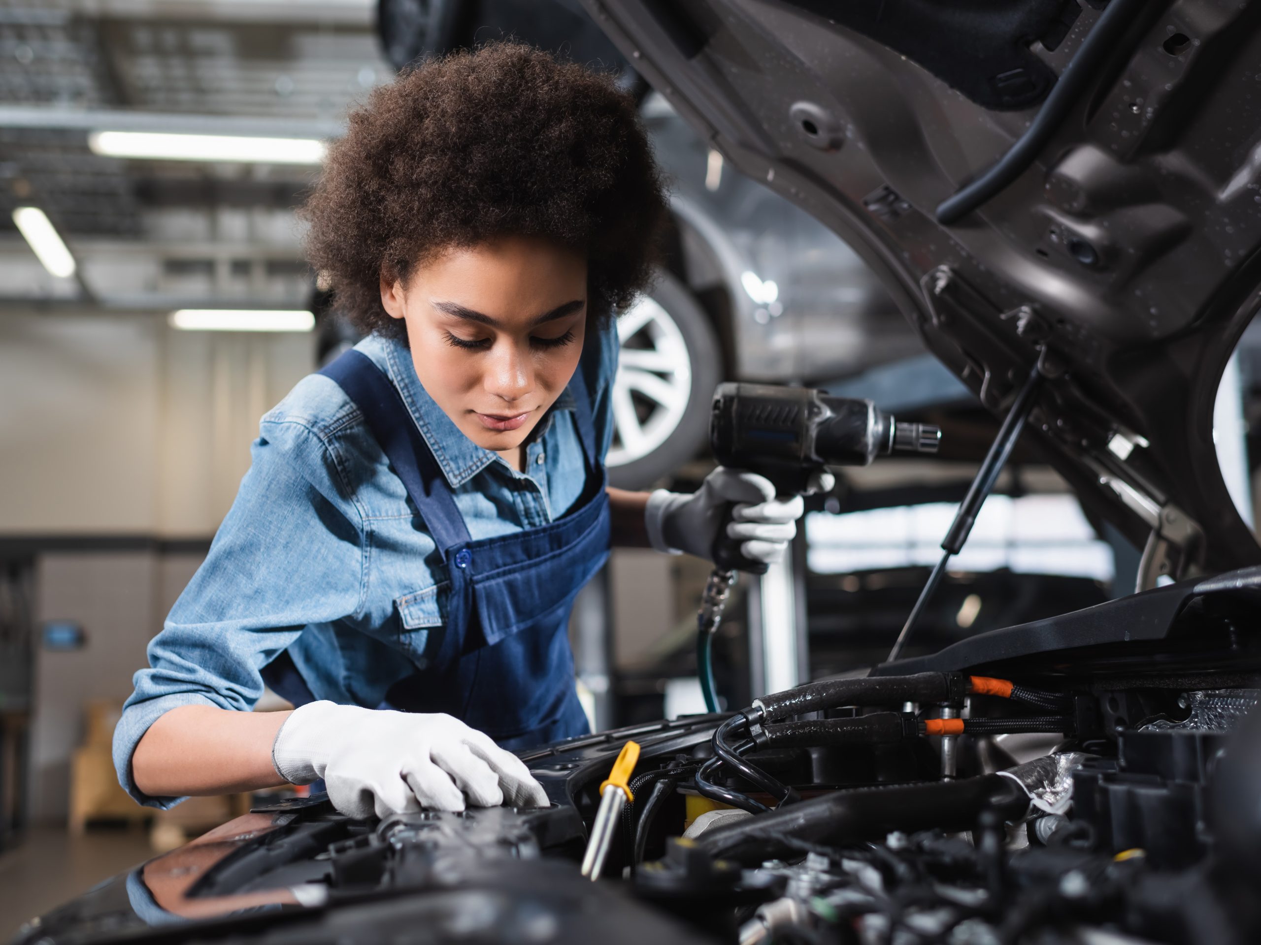A mechanic holding a pneumatic socket wrench working under the hood of a car. 