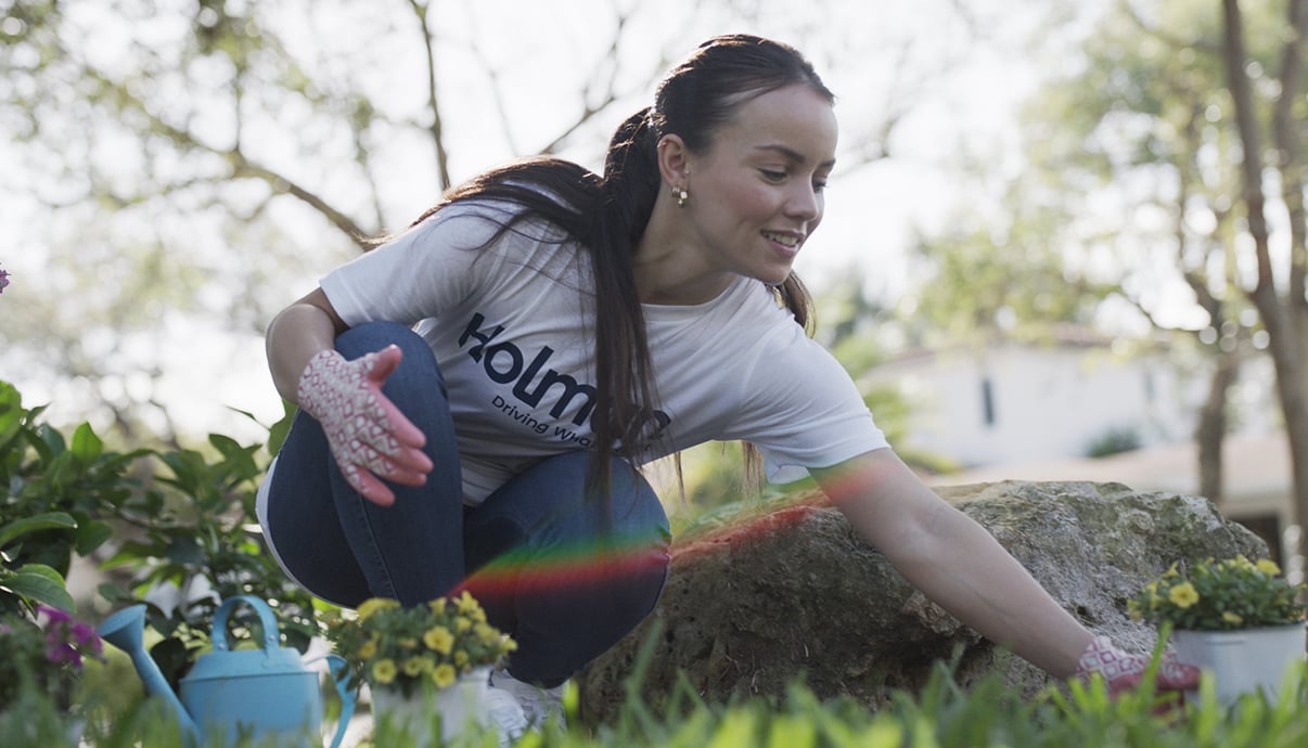 A woman gardening wearing a white shirt with a blue Holman logo.