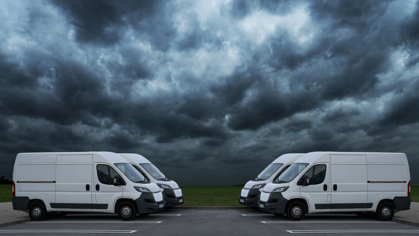 Two rows of white vans parked in stormy weather.