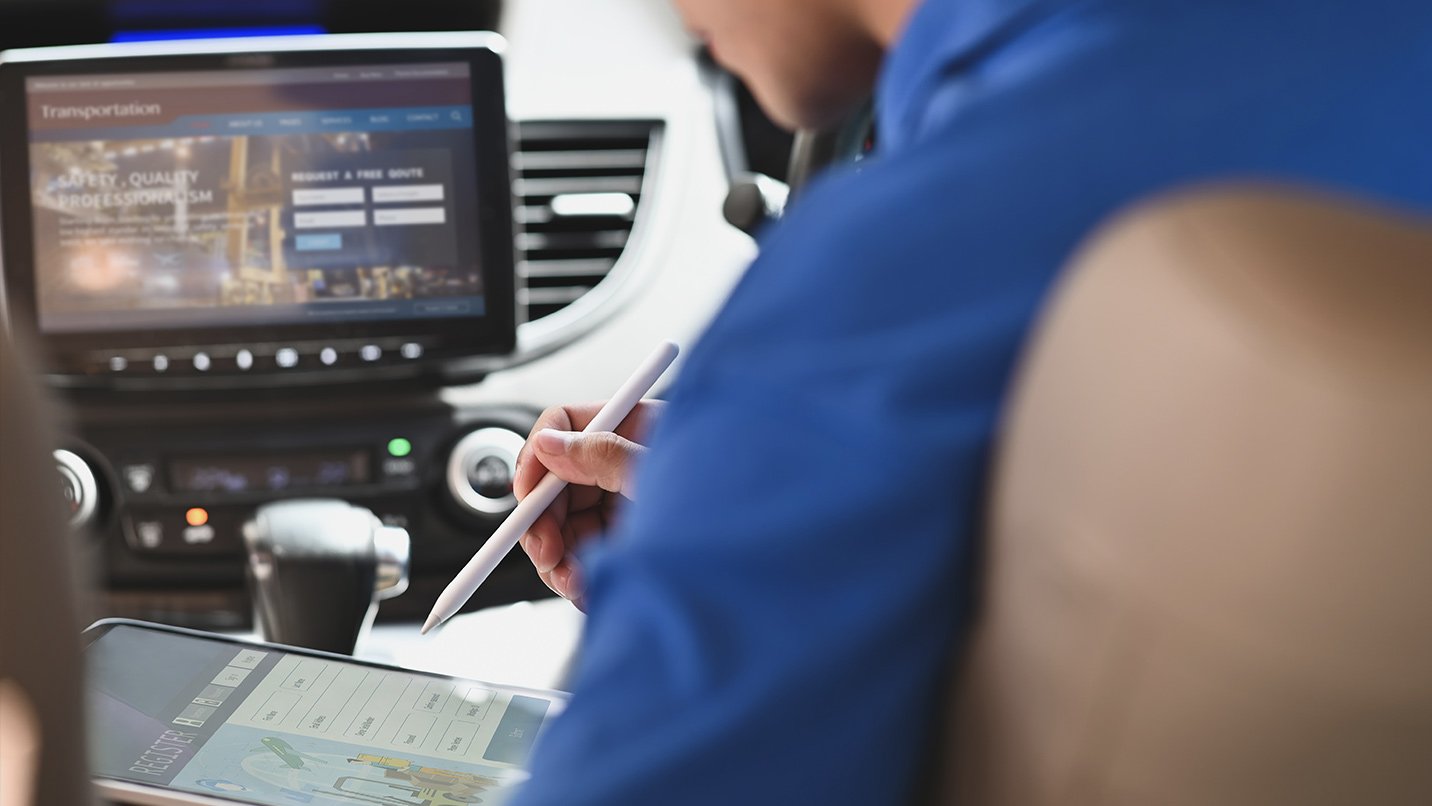 Driver in parked car filling out a form on a tablet with stylus.