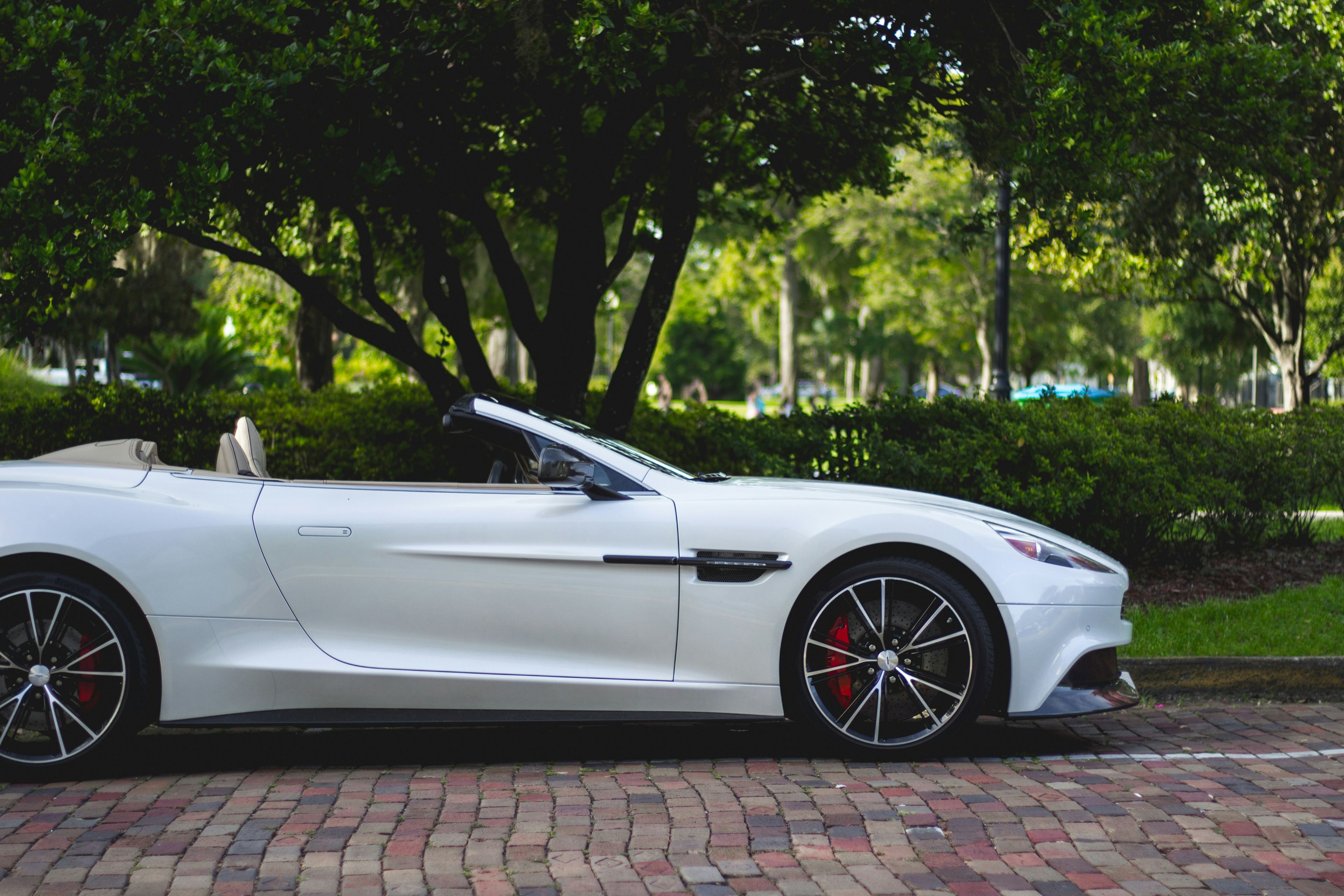 White Aston Martin convertible on brick paving with green trees behind