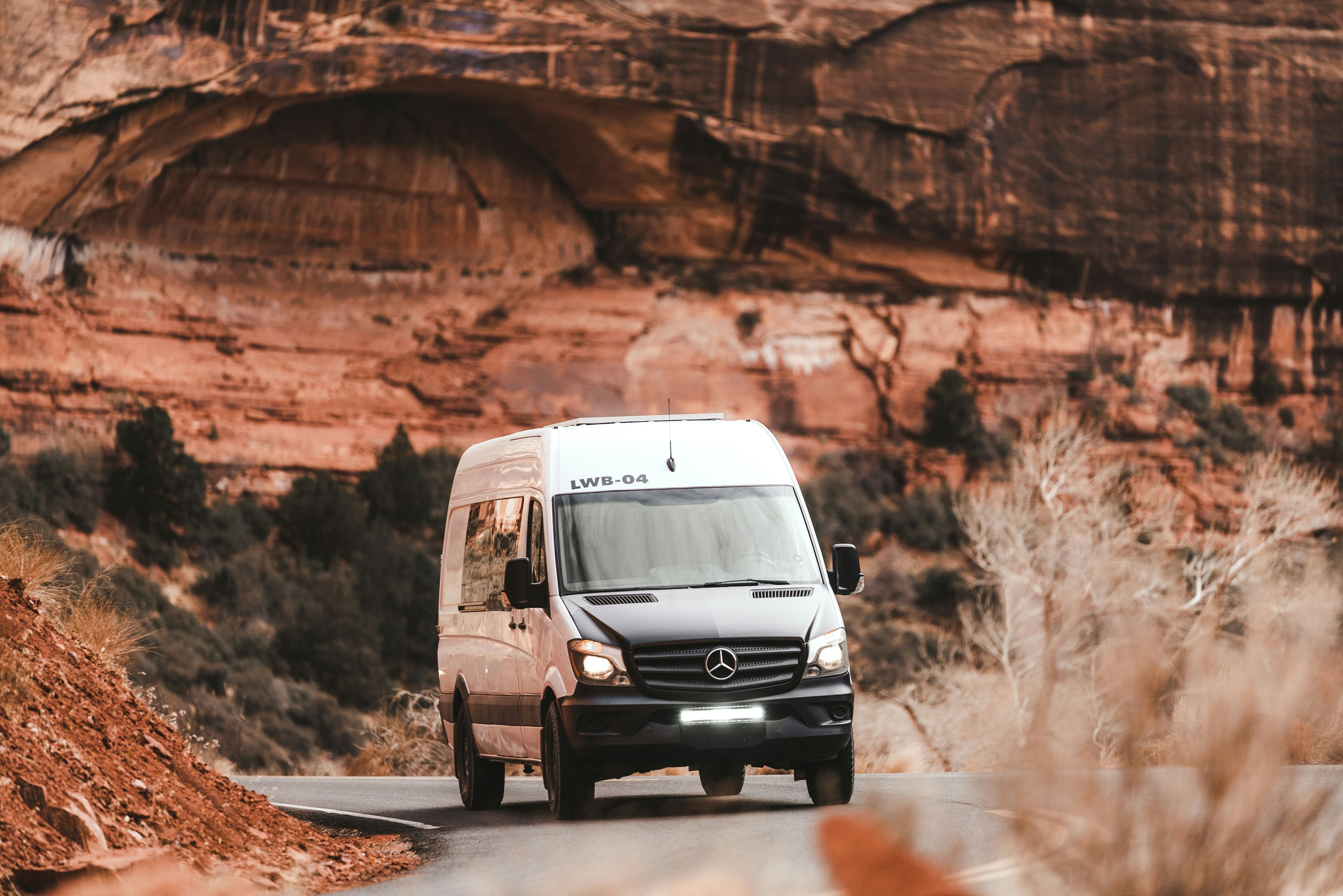White Mercedes Sprinter van driving a road through a red-rock canyon