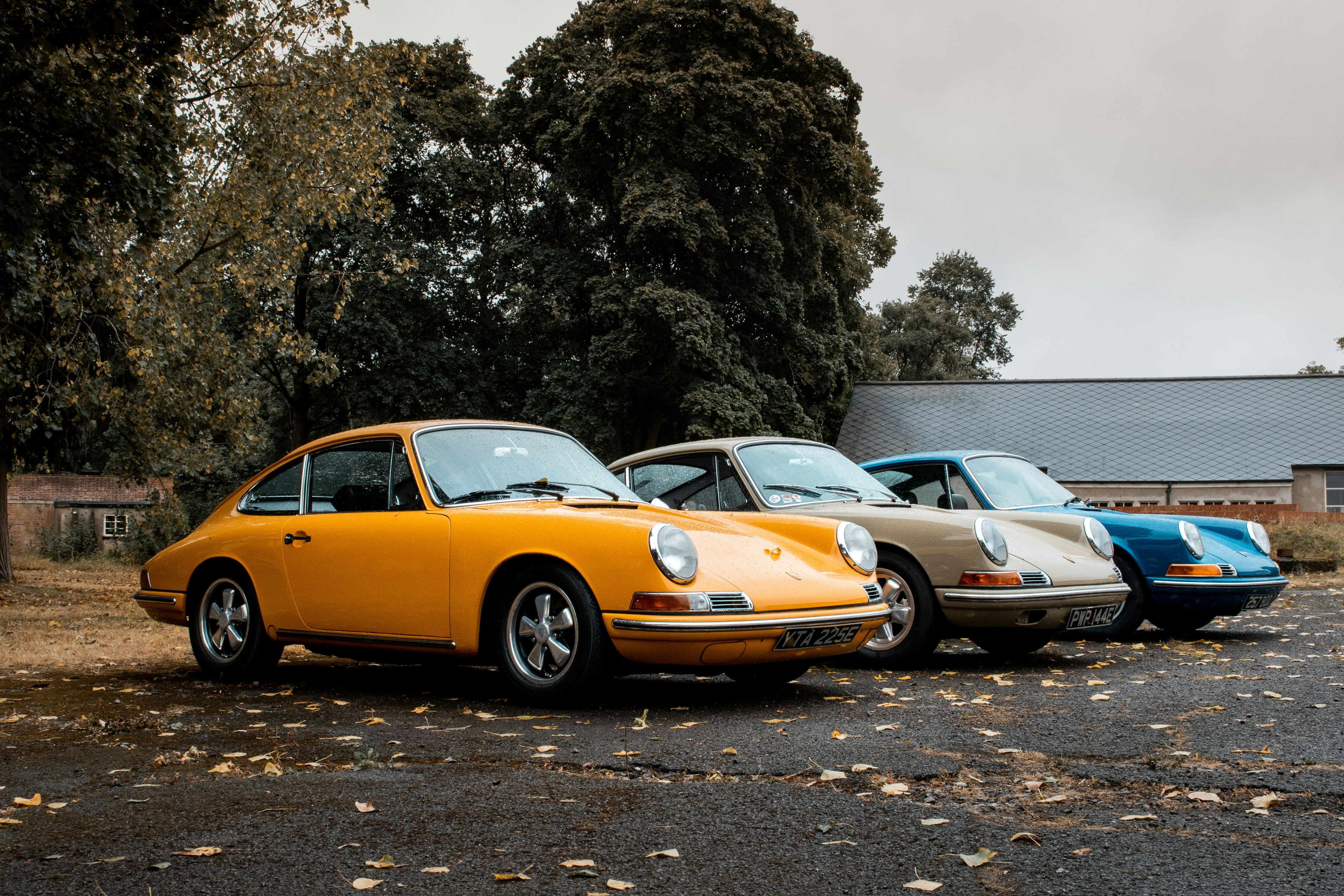 Three classic early Porsche 911s lined up on gravel with UK plates