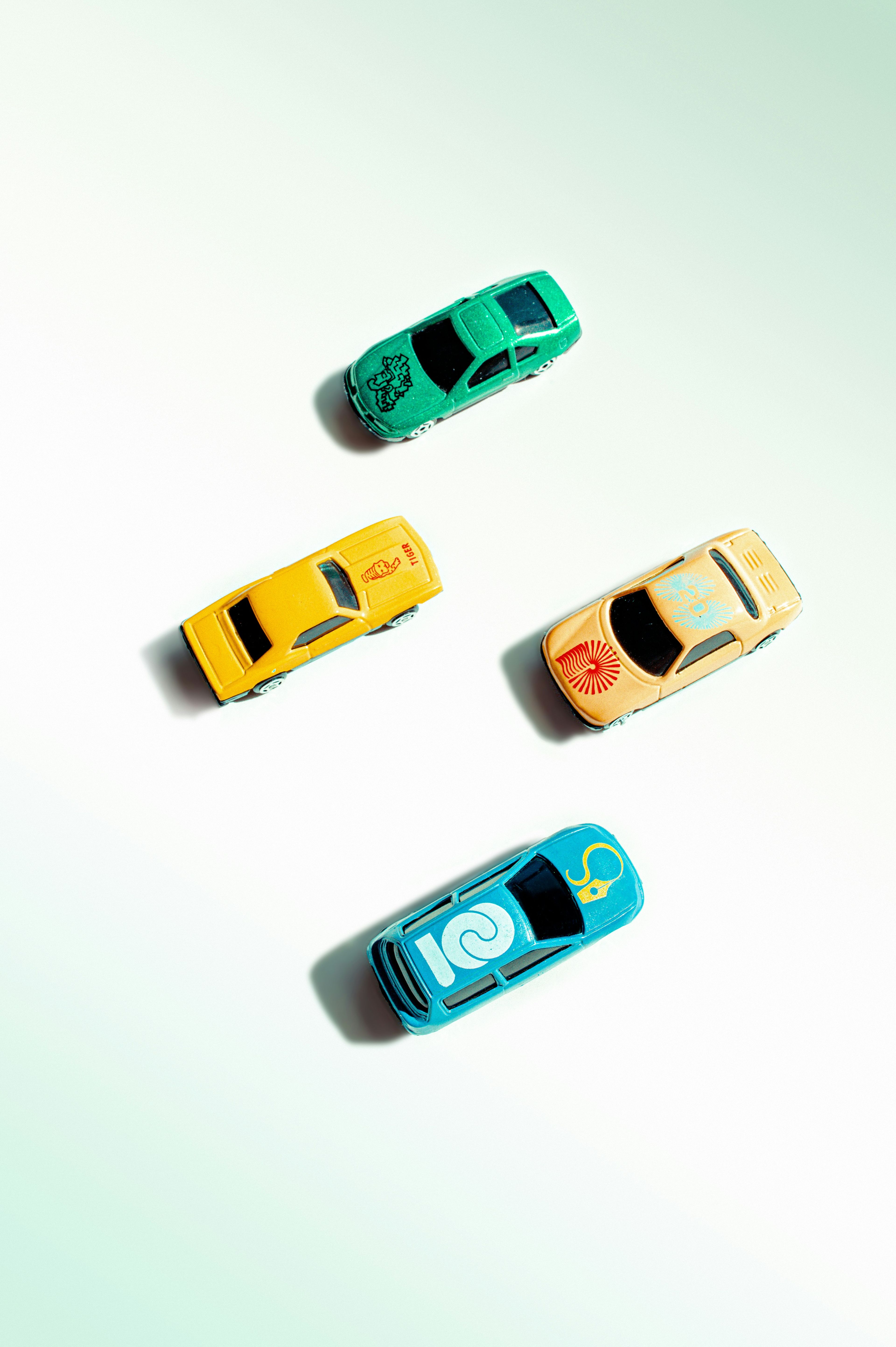 Top-down flat-lay of four colourful vintage toy cars on pastel background