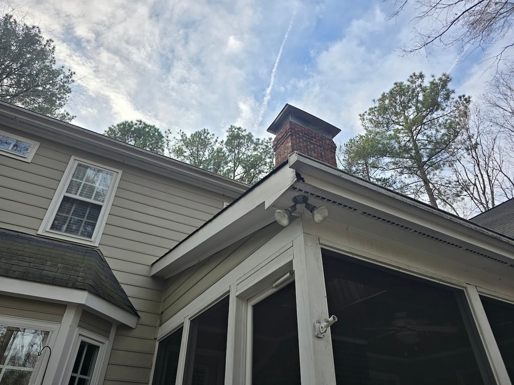 A detailed view of a repaired fascia board corner on a rear porch located on Bayswater Trail in the Brookhaven neighborhood of Raleigh, NC. The image captures the transition from structural wood repair to the final painted finish, showcasing professional carpentry and a seamless, weather-resistant coating.