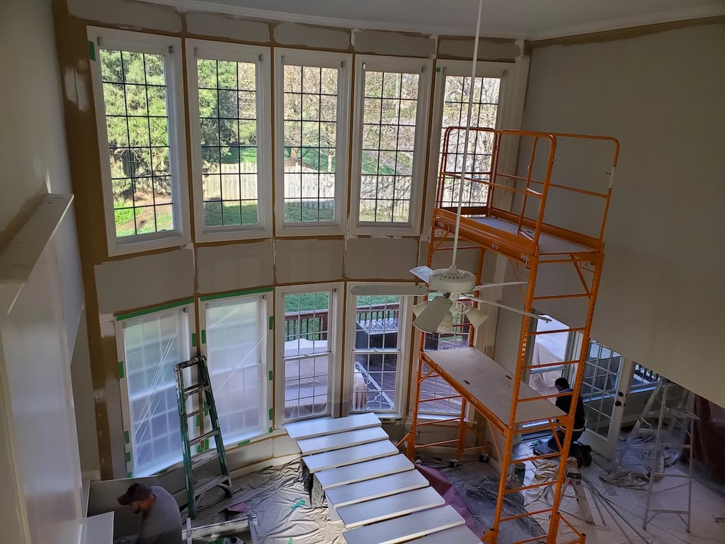 Professional painters using scaffolding to paint high-elevation walls and vaulted ceilings in a two-story living room in Apex, NC, near Beaver Creek Commons to ensure a uniform, professional finish.