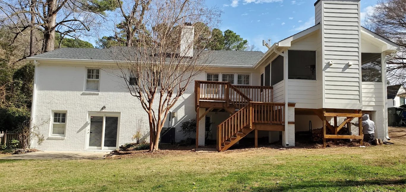 Rear view of a white brick home in Raleigh’s North Hills neighborhood after a professional masonry coating by A Touch of Color Painting & General Contracting, featuring a technician performing final touch-ups on the breathable mineral finish.