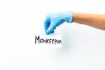 hand with blue surgical glove holding sign with the word monkeyvox