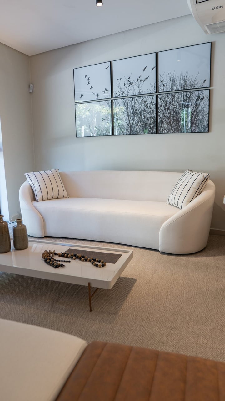 Sofá de três lugares em tecido claro posicionado em sala de estar com iluminação natural e mesa de centro