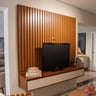 Sala de estar com painel de TV em madeira escura, sofá cinza e iluminação ambiente, decoração contemporânea