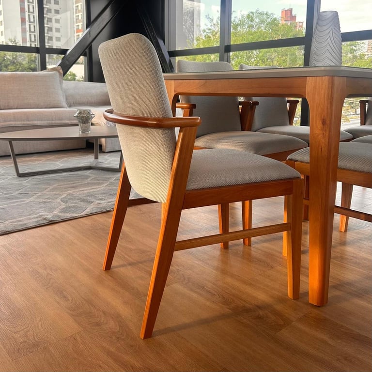 Cadeira Betina com braços em madeira, encosto alto e assento estofados em tecido bege, junto à mesa Betina de tampo off-white