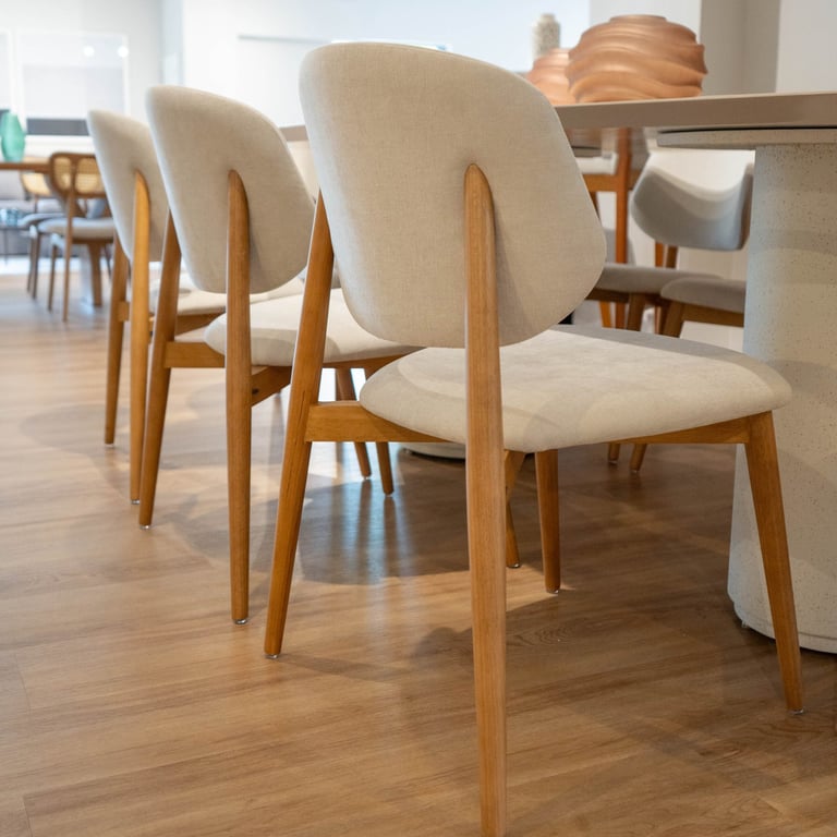 Três cadeiras Brisa em madeira tauari com assento e encosto estofados em tecido off-white, alinhadas junto a mesa de jantar