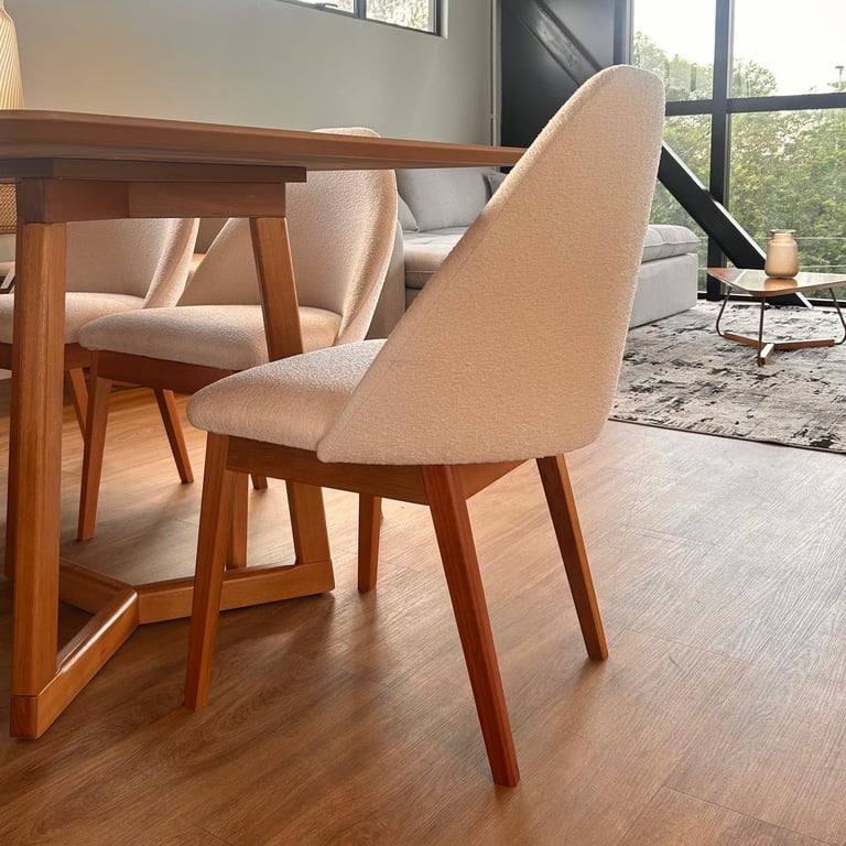 Cadeira Carol em madeira cinamomo com assento e encosto alto estofados em tecido bouclé off-white, junto a mesa de jantar