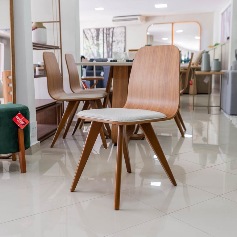Cadeira Lidiane com encosto curvo em madeira nogueira e assento estofado claro, em showroom