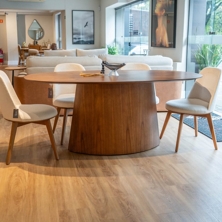 Mesa de jantar Arezzo com tampo oval em lâmina de madeira e base cônica central, acompanhada de cadeiras estofadas off-white