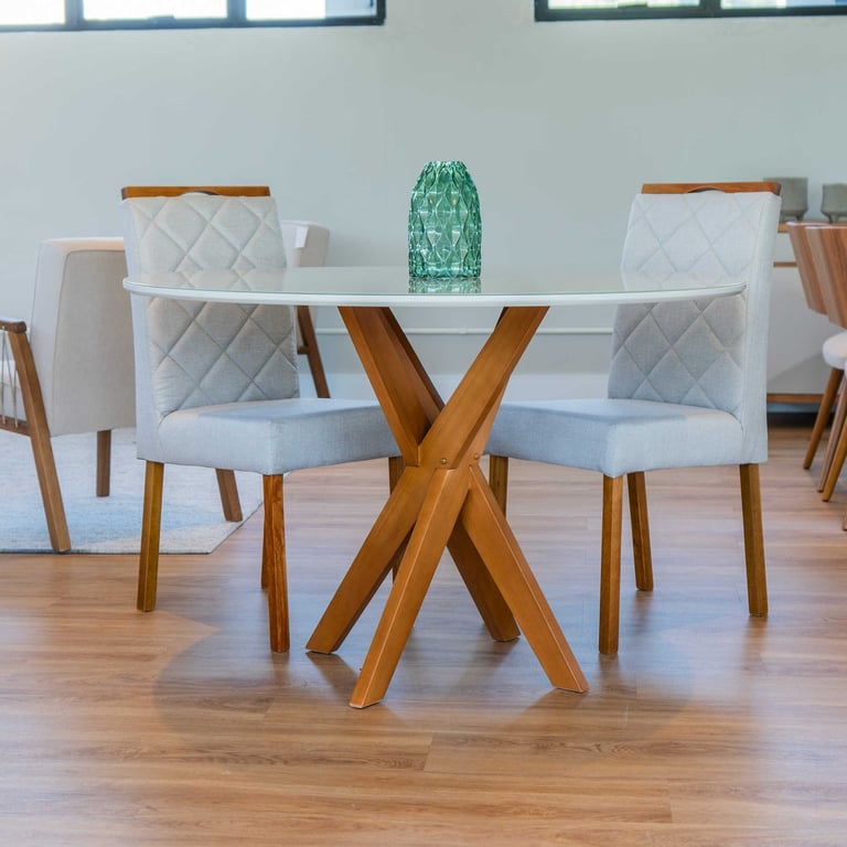 Mesa de jantar Joy redonda com tampo de vidro branco sobre base de pernas cruzadas em madeira, com cadeiras estofadas claras matelassê