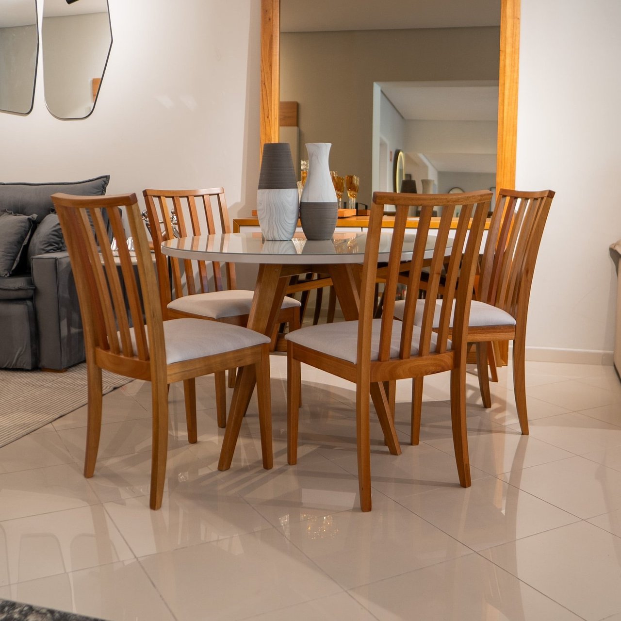 Mesa de jantar redonda Aspen com tampo off-white e base de madeira em cavalete, cercada por cadeiras de madeira com encosto ripado